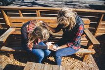Girl friends praying on a park bench.