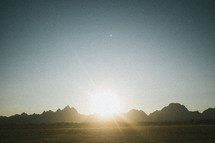 sunburst over a field and mountain peaks 