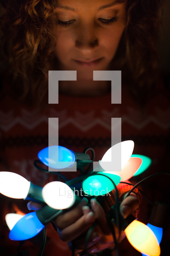 a woman holding a string of Christmas lights in darkness 