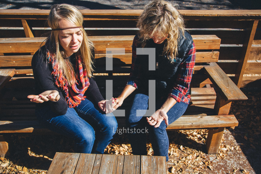 women sitting on a bench holding hands in prayer 