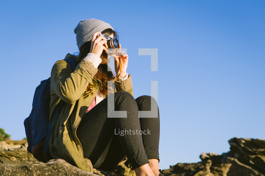 woman sitting on rocks taking pictures with a camera 