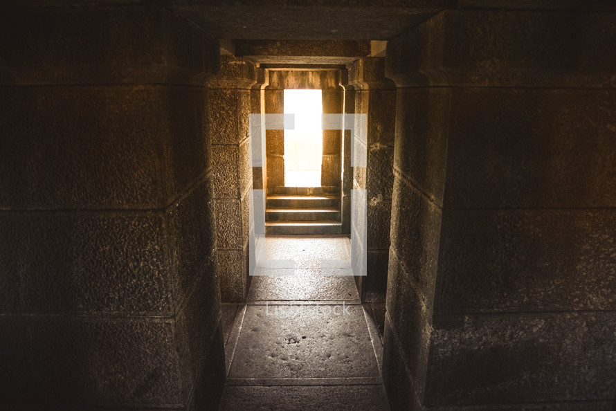 Bright sunlight at the end of a stone hallway.