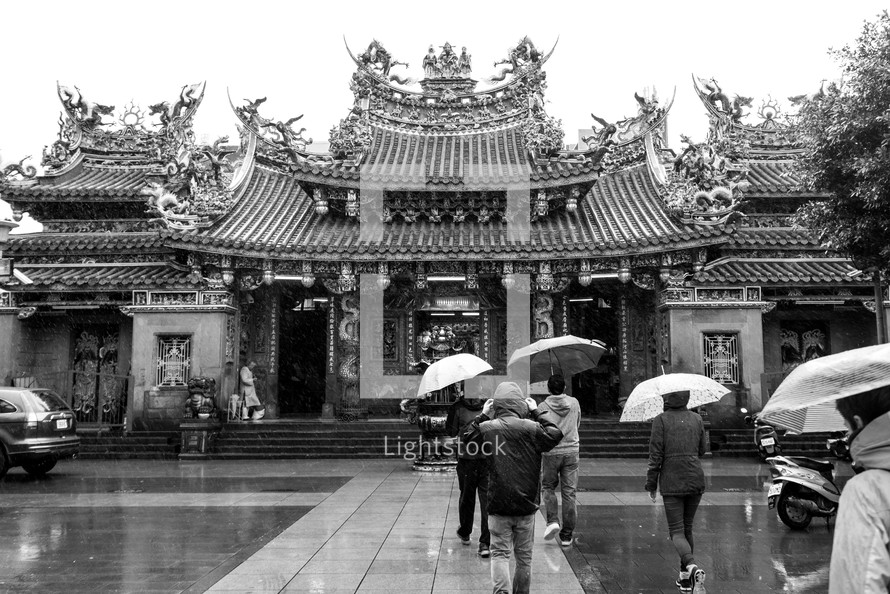People walking with umbrellas towards a temple 