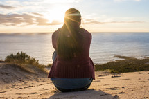 woman with her back to the camera sitting on a beach in a sweater 