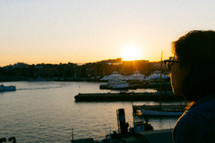 a woman looking out at boats in a harbor at sunset 