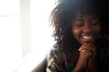 An African American woman with praying hands and a smile 