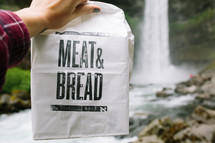 meat and bread paper sack near a waterfall 