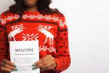 woman in an ugly Christmas sweater holding an invitation 