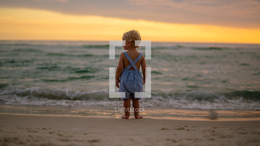 toddler boy standing on a beach at sunset 