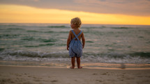 toddler boy standing on a beach at sunset 