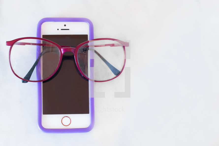 Red reading glasses on a cellphone on a solid white background. 