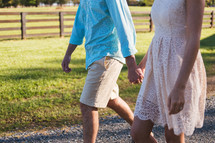 Couple holding hands walking on a gravel road.