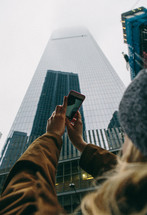 woman taking a picture of a skyscraper with her phone 
