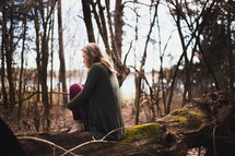 woman sitting on a fallen tree in a forest deep in thought 