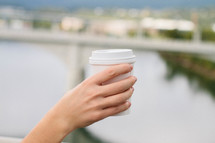 a woman holding up a paper coffee cup 
