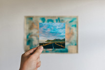 holding up a photograph of a highway along a shoreline 