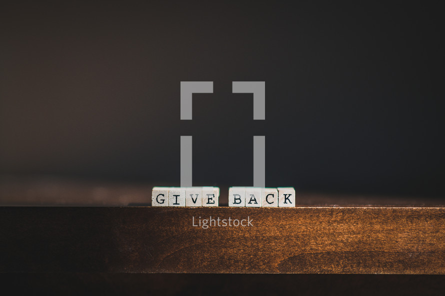 Wooden tiles spelling "Give Back" on wooden table