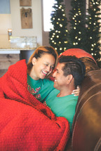 a couple snuggling under a blanket at Christmas 