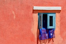 Blue curtains hang from a window set in an orange painted wall 