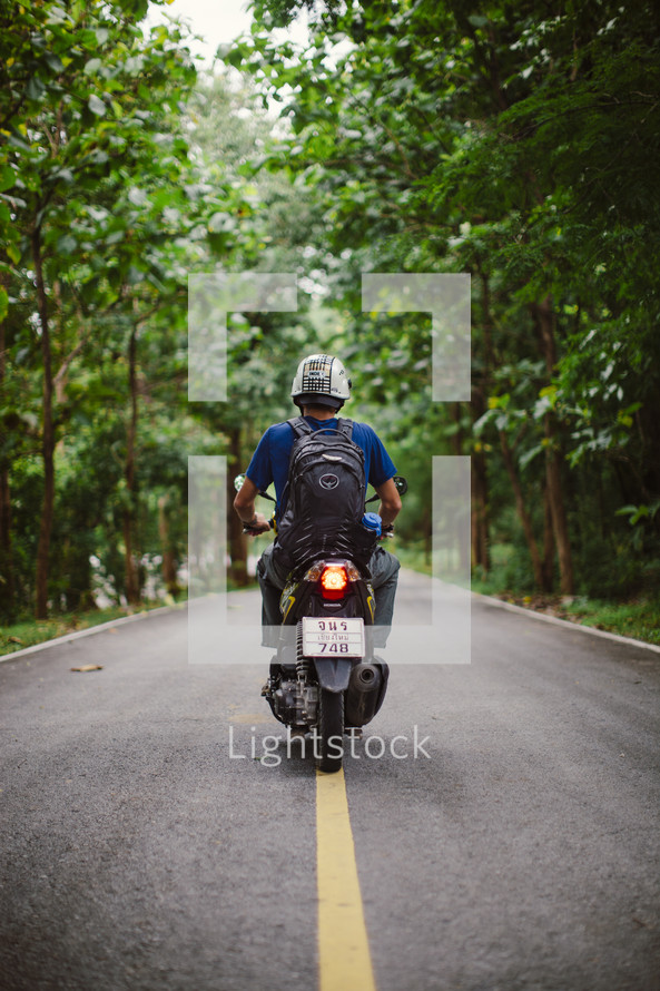 man riding a motorcycle on the center lines of a road 