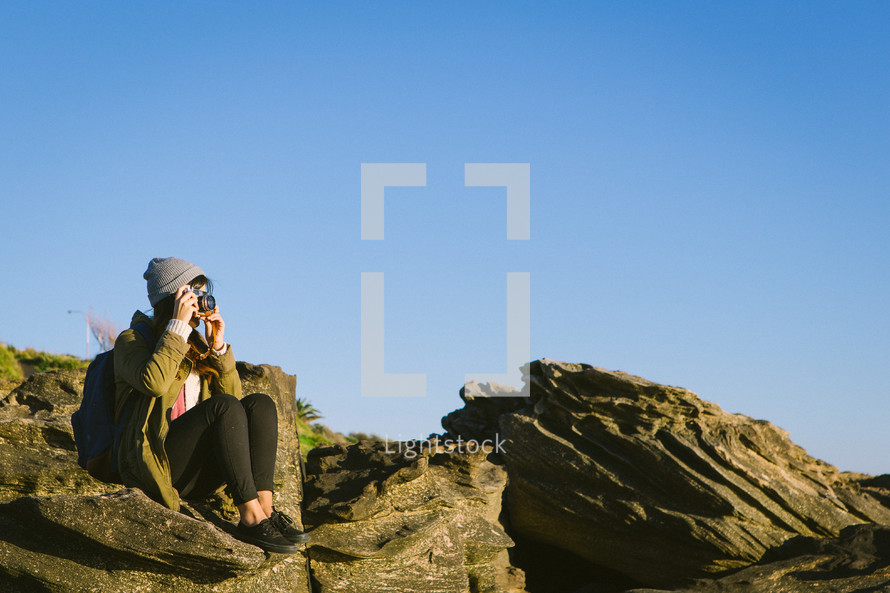 woman sitting on a rock taking pictures with a camera 