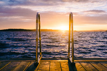 Sunset over water with a wooden dock and a ladder.