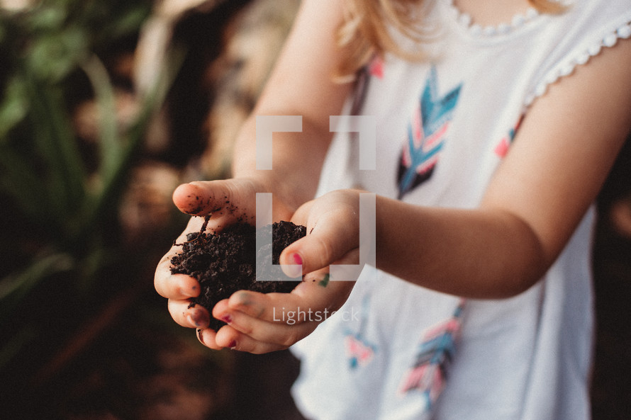 toddler girl with cupped hands full of potting soil 