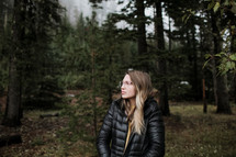 a woman in a coat standing alone in a forest 