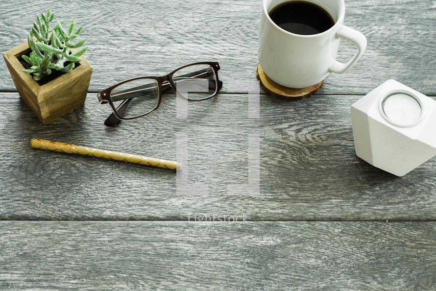 house plant, pen, reading glasses, candle, coffee, and coaster on a table 