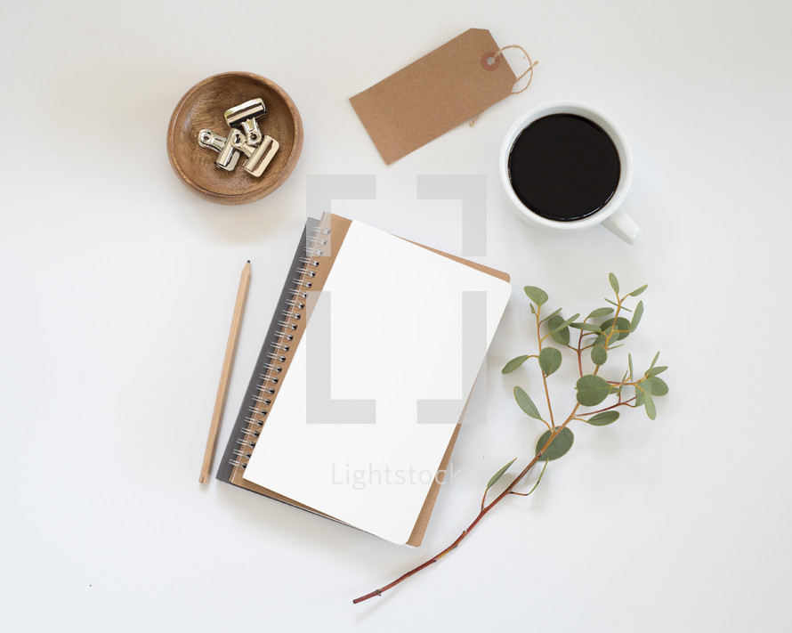 stack of journal, eucalyptus twig, pencil, clips in a bowl, gift tag, and coffee cup 