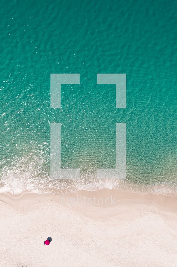 Vertical image of the water, beach, and an umbrella