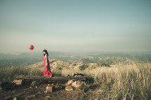 a woman on a mountaintop in a red dress holding a red balloon 