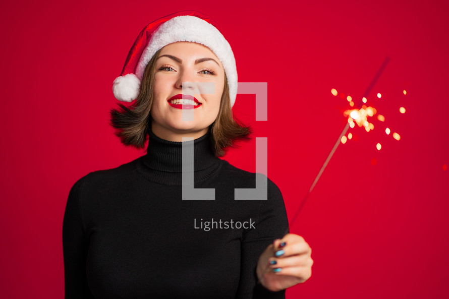 Trendy hipster girl in Santa hat with bengal sparkler fire on red background.