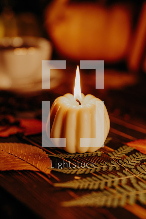 Autumn background. Pumpkin candle, orange fallen leaves. Flat lay. Cozy ambiance of fall, candle burning. Seasonal promotions or tranquil visual storytelling. 