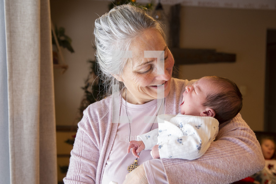 Grandmother holding yawning newborn baby and smiling