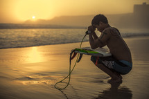 squatting surfer with his head bowed in prayer over his surfboard 