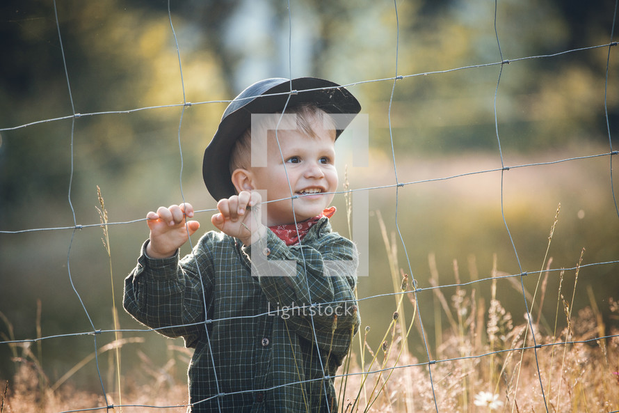 Cute Toddler Kid in Western Cowboy Outfit behind the Wire Fence