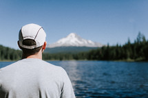 man standing in front of a mountain lake 