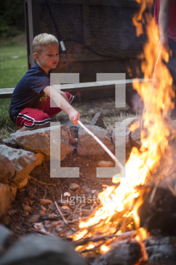 A young boy poking a campfire with a stick.