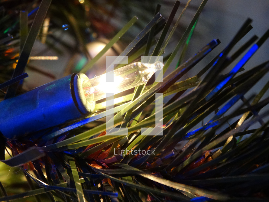 Close up of golden white Christmas tree light against pine needles on Christmas tree