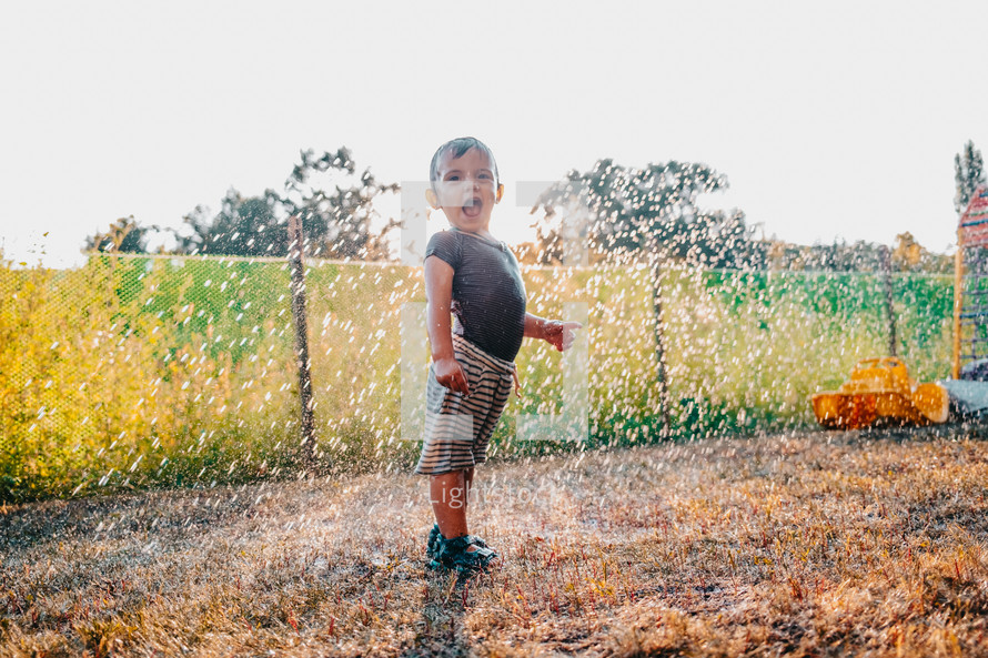 Happy adorable toddler boy having fun under rain. Baby laughs, he is very glad weather. High quality photo