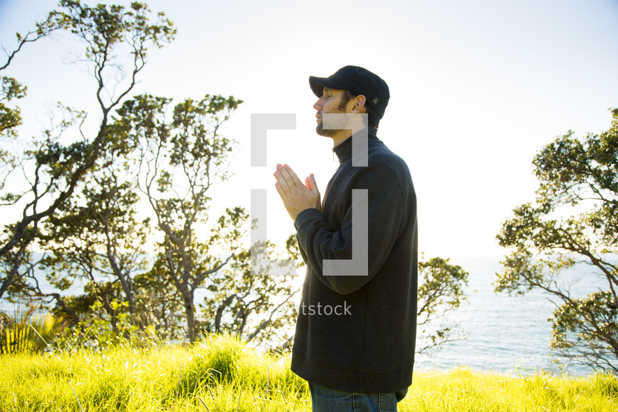 man standing outdoors with praying hands in reverent prayer to God 
