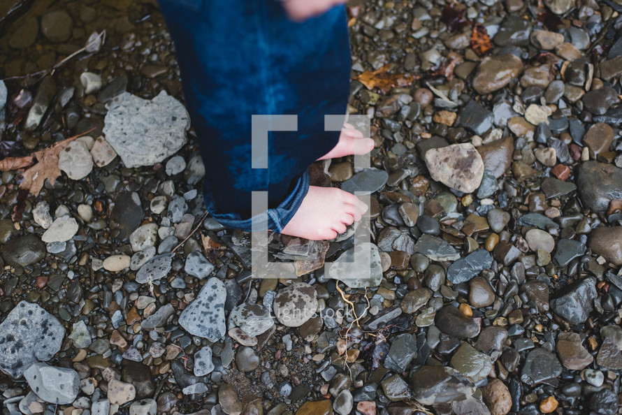 a barefoot child standing on pebbles 