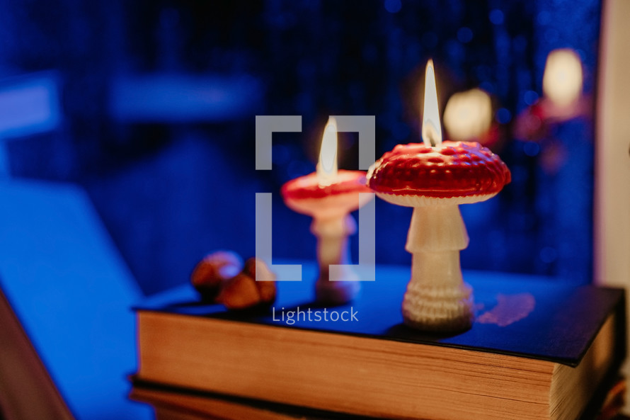 Autumn background. Mushroom candles burning on stack old books. Quiet moments. Flat lay. Cozy ambiance of fall. Seasonal promotions or tranquil visual storytelling. 
