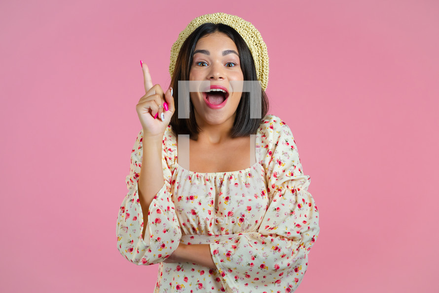 Portrait of young thinking pondering woman having idea moment pointing finger up on pink studio background. Smiling happy showing eureka gesture