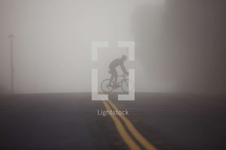 man riding a bike across the street under thick fog
