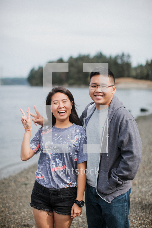a couple standing on a river shore giving peace signs 