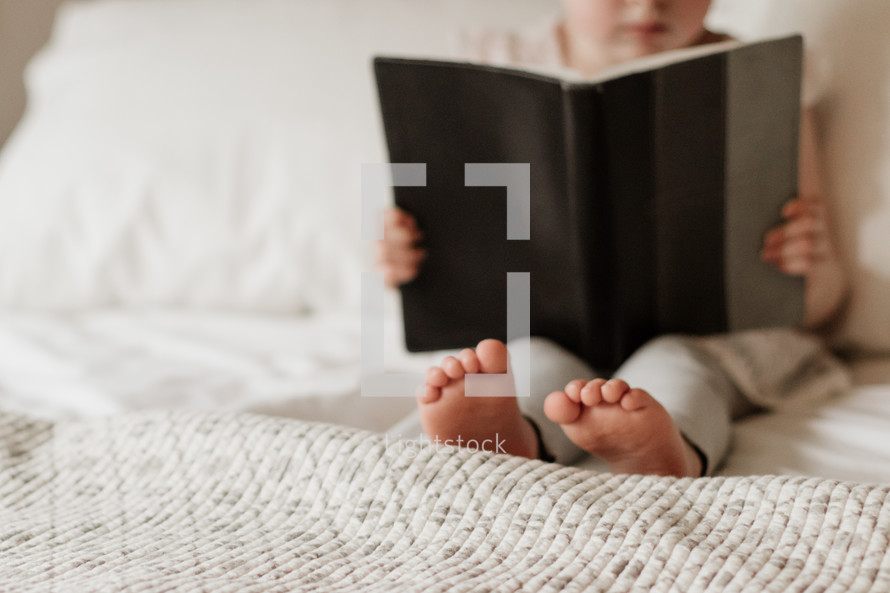 toddler reading a book in bed 
