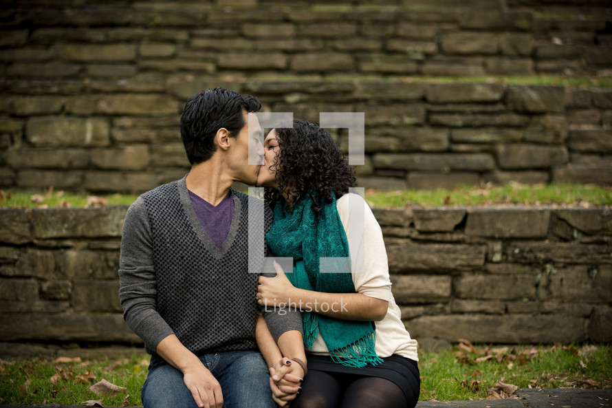 man and woman sitting outdoors kissing