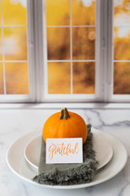 Thanksgiving place setting with the word grateful in front of a kitchen window
